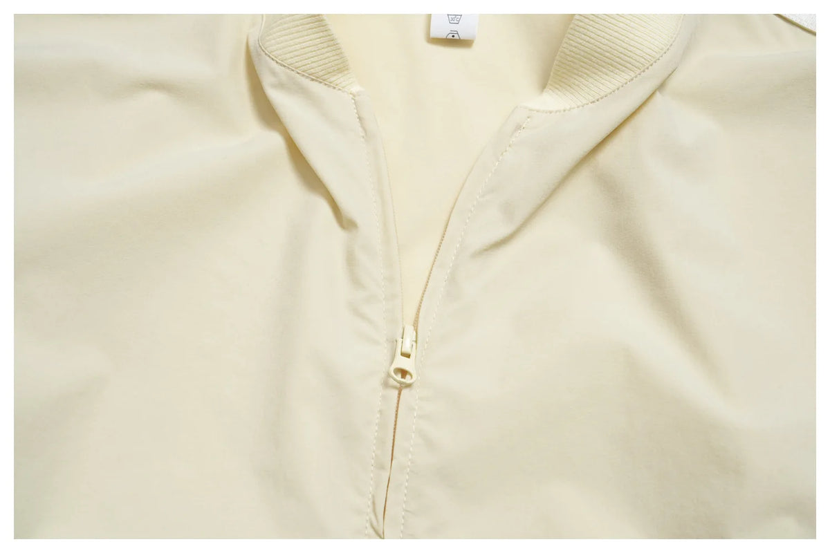 Women’s zip-up athletic jacket, light cream front with centered gold zipper