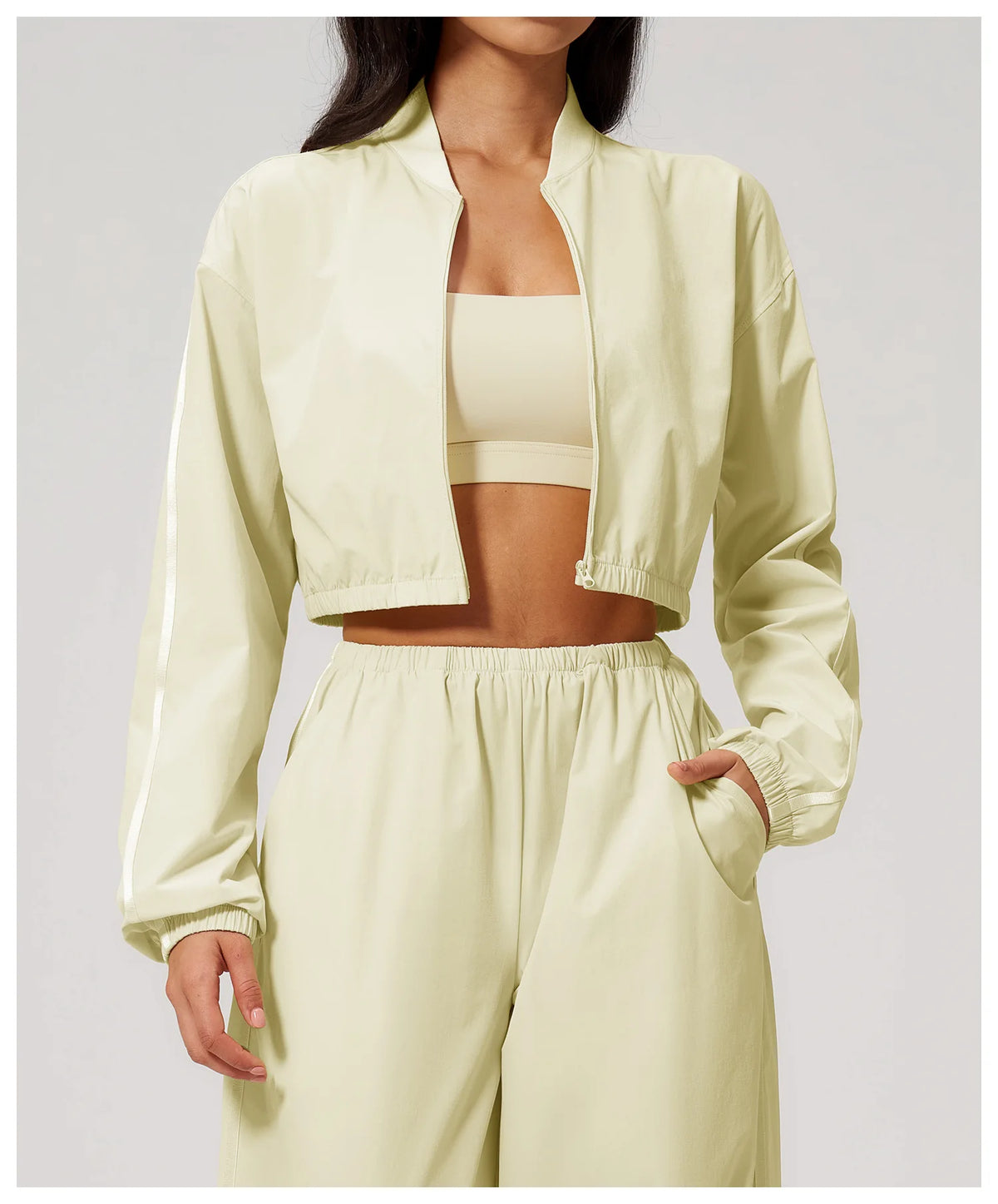 Women’s almond yellow zip-up cropped jacket with long sleeves over a sports bra.