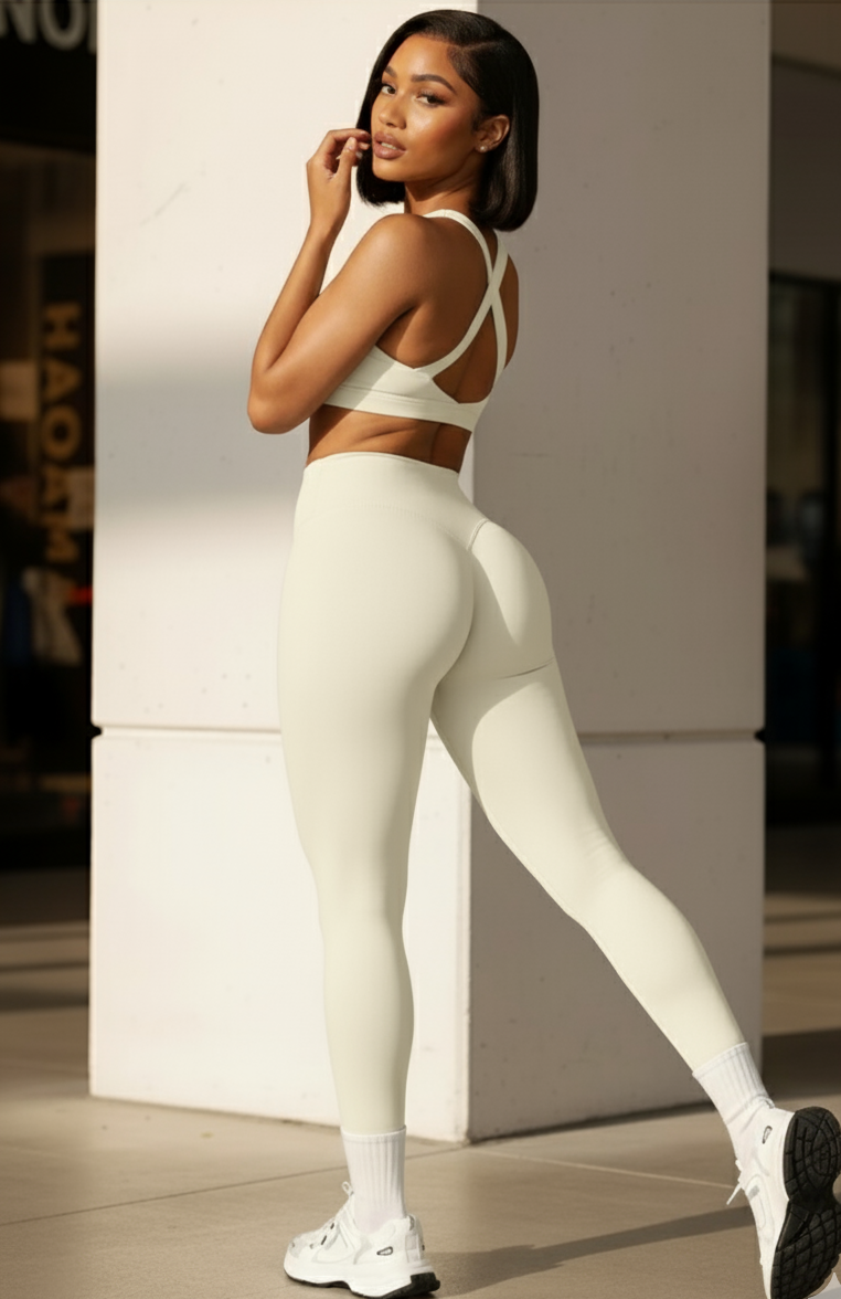 Woman in a white sports bra and leggings standing against a light-colored wall.
