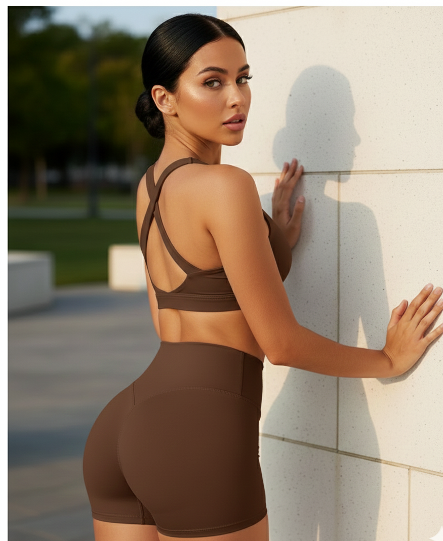 Woman in brown athletic wear standing against a wall with a blurred outdoor background