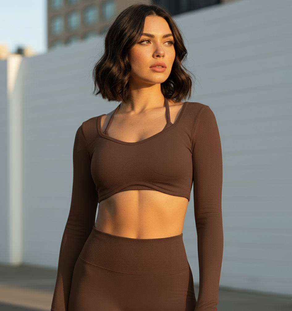 Woman wearing a brown long-sleeve athletic top and leggings against a light-colored wall.