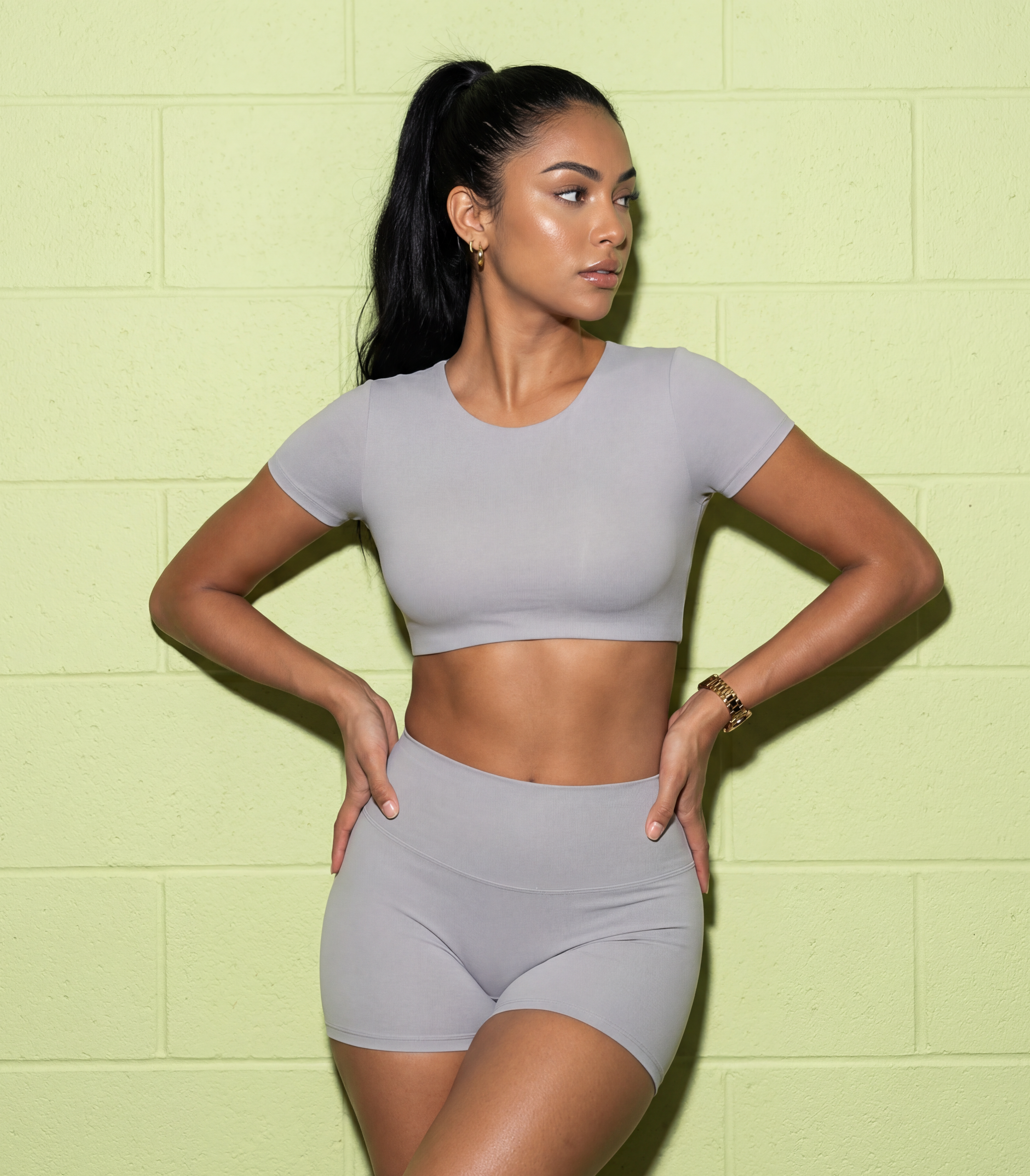 Woman wearing a gray athletic outfit against a light green wall