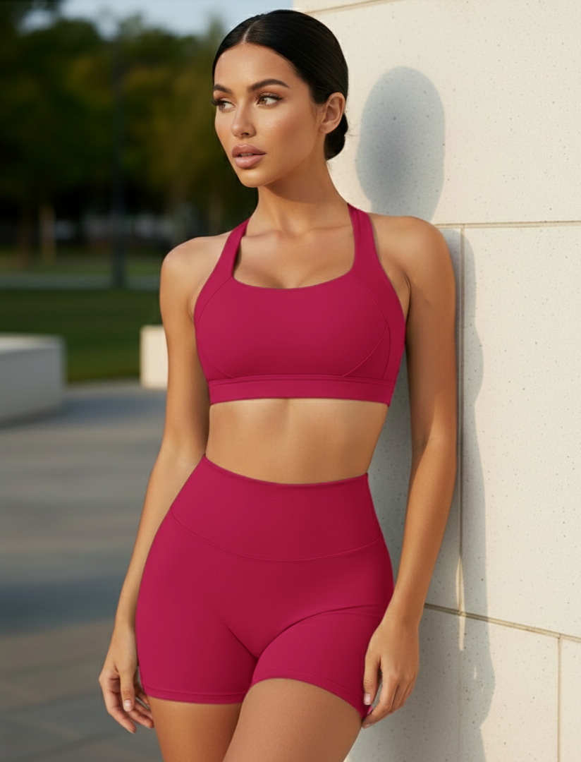 Woman wearing a pink athletic outfit leaning against a wall outdoors.