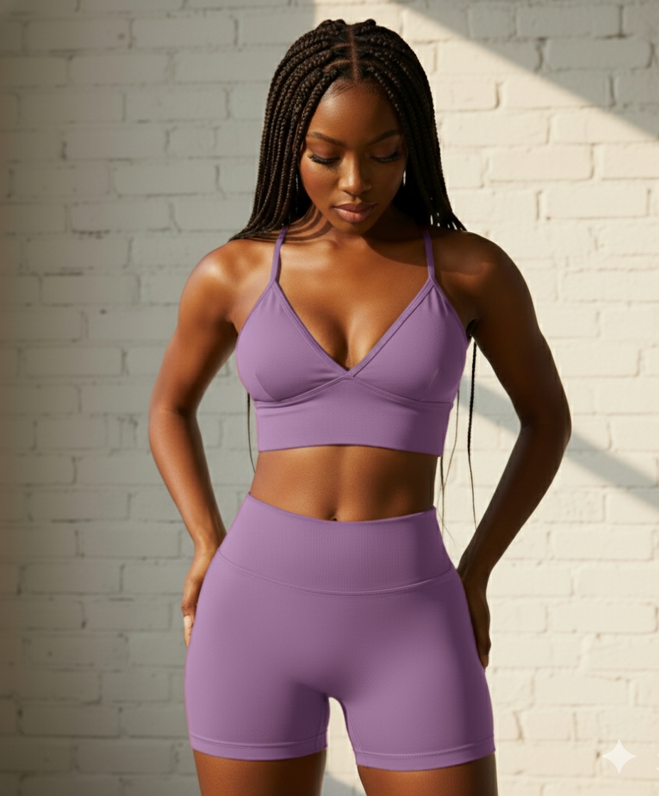 Woman wearing a purple sports bra and shorts set against a white brick wall.