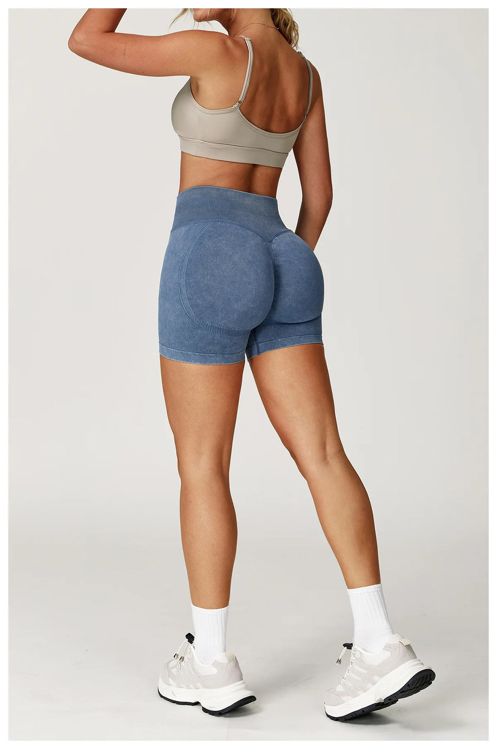 Xooie Fit acid wash workout shorts in blue worn by woman with beige sports bra and white sneakers