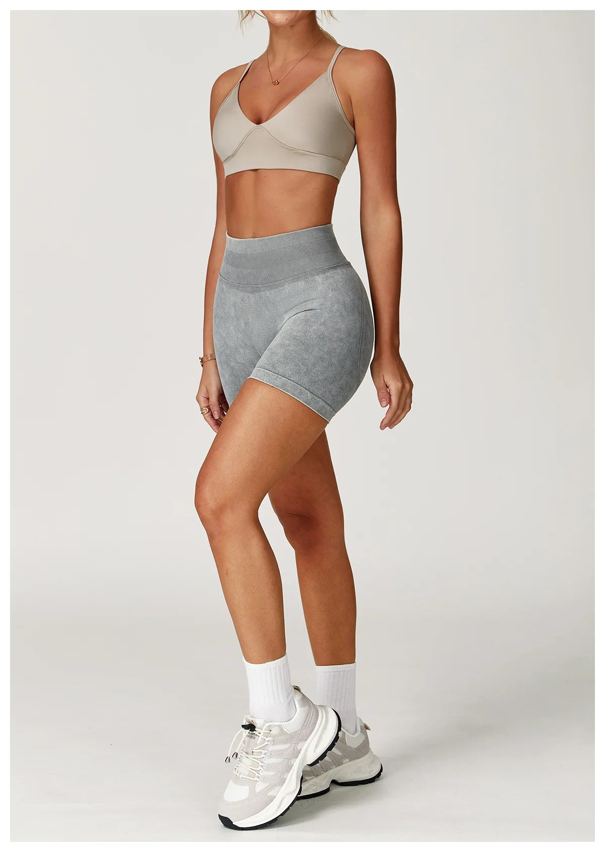 Xooie Fit acid wash workout shorts in gray worn with beige sports bra and white sneakers