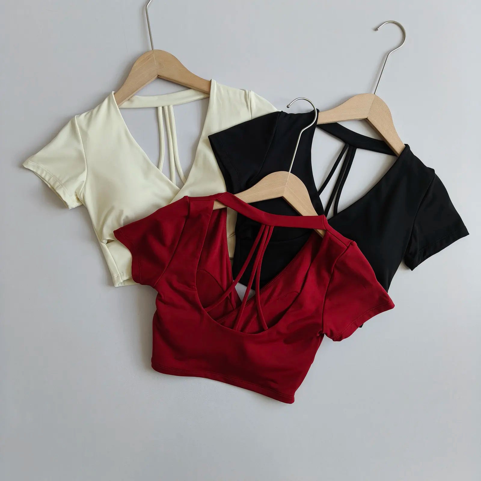 Three cross-over crop tops on hangers in cream, black, and wine red