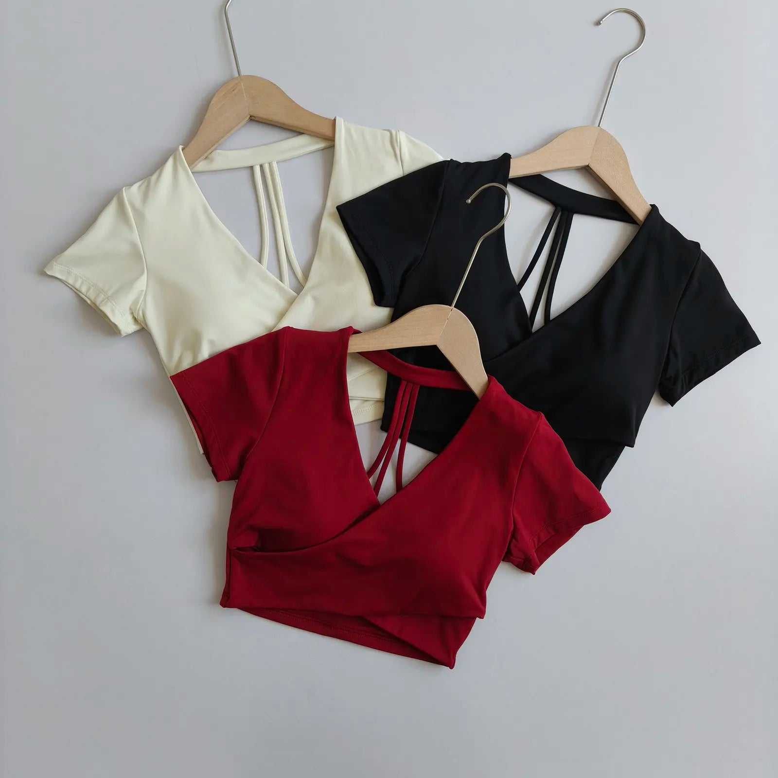 Mixed-color cross-over crop tops on hangers: cream, black, and wine red