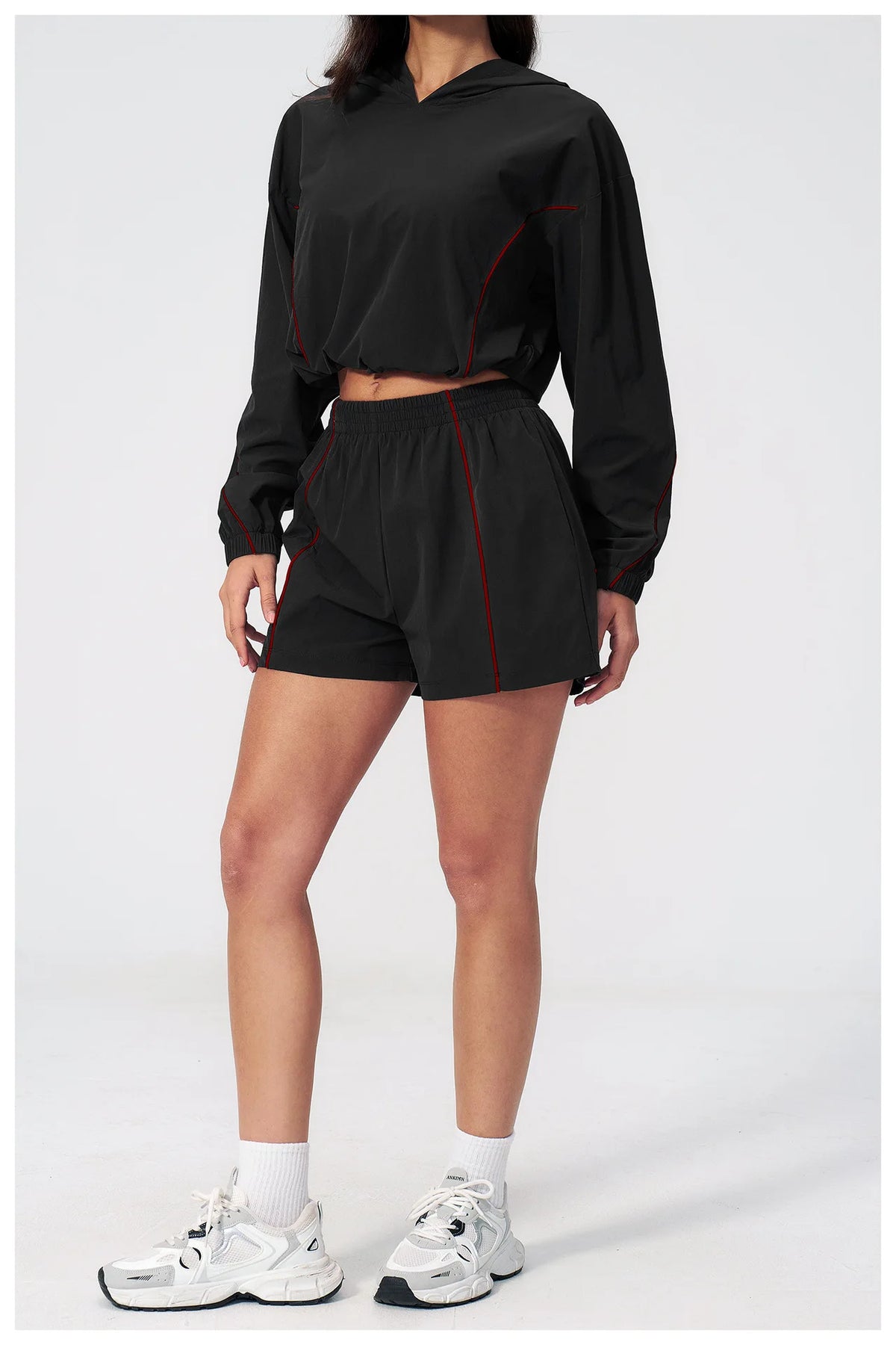 Women’s hooded sports set in black, front view with red piping on jacket and shorts