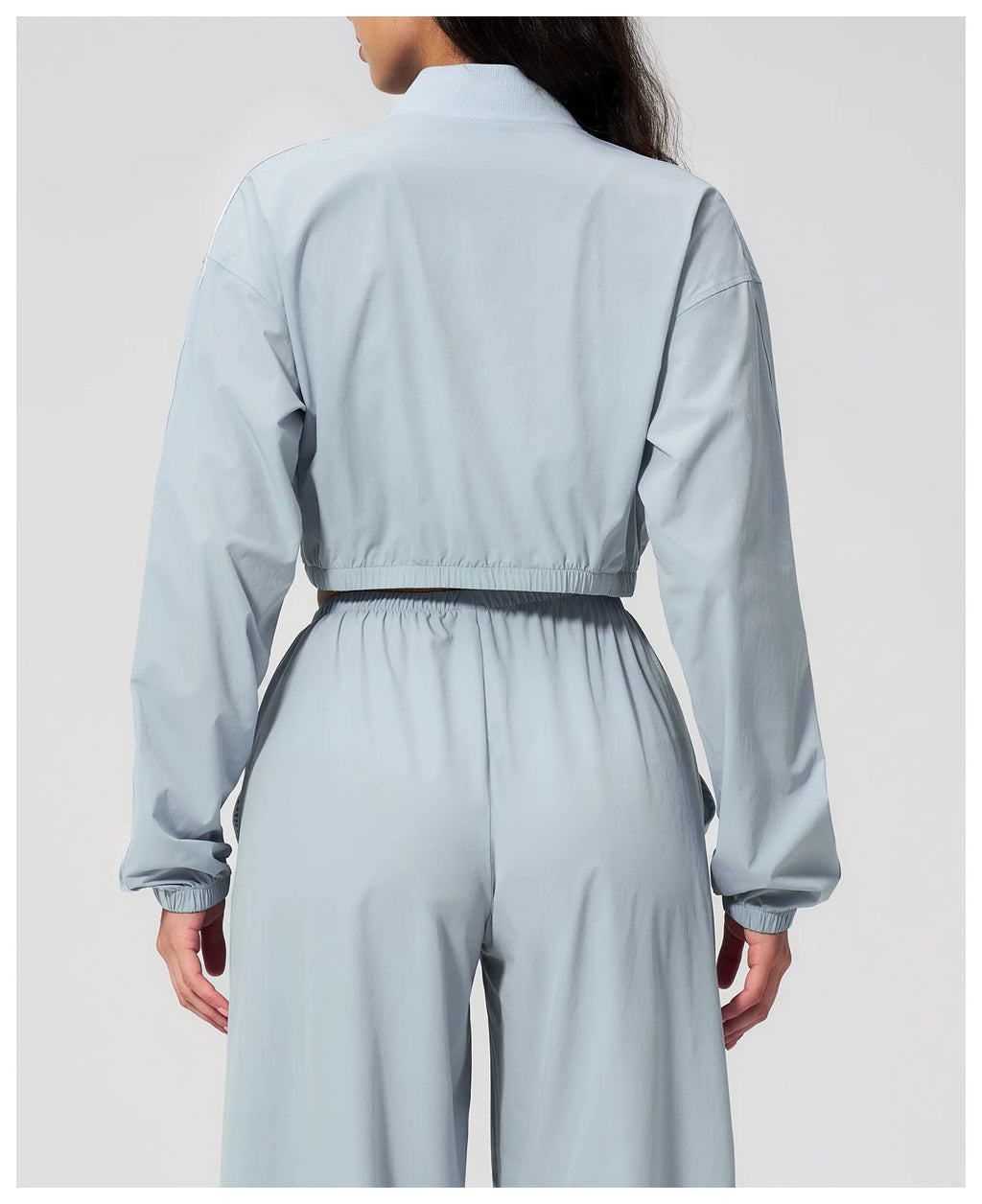 Women’s cropped sky blue zip-up jacket, back view with elastic waist hem.