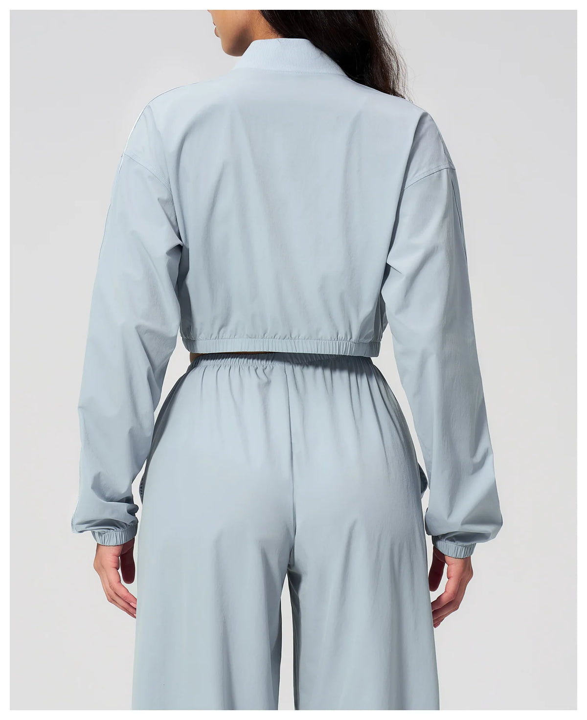 Women’s cropped sky blue zip-up jacket, back view with elastic waist hem.