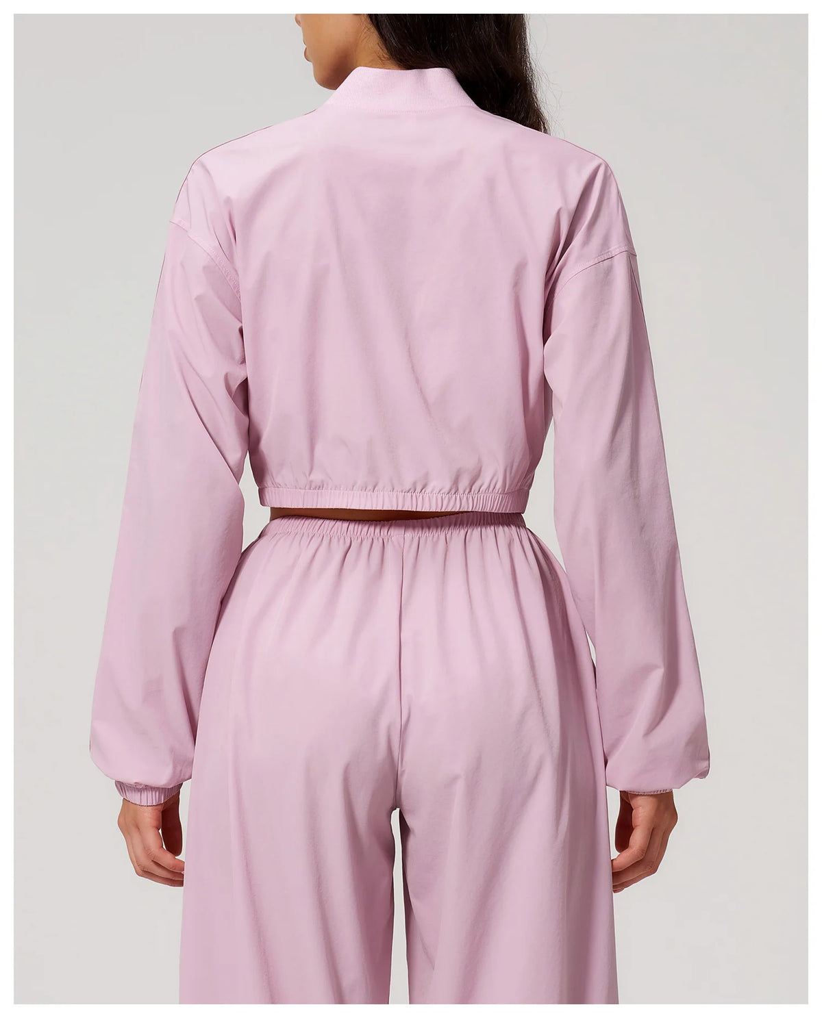 Women’s light pink zip-up cropped jacket from back with elastic waistband and long sleeves.