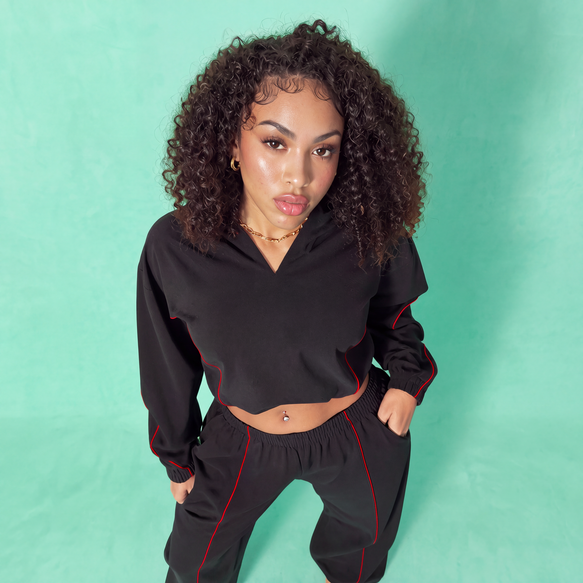 Black crop hoodie and jogger pants set with red stripe accents, close-up