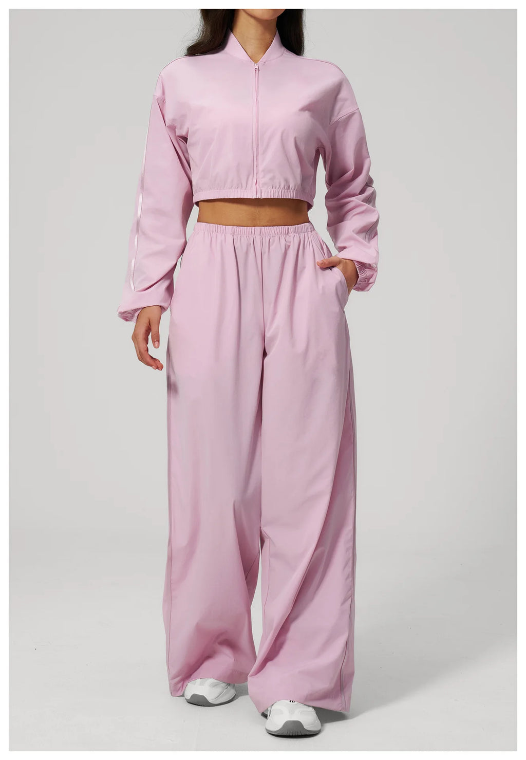 Women’s cropped light pink zip-up jacket with long sleeves and matching wide-leg pants.