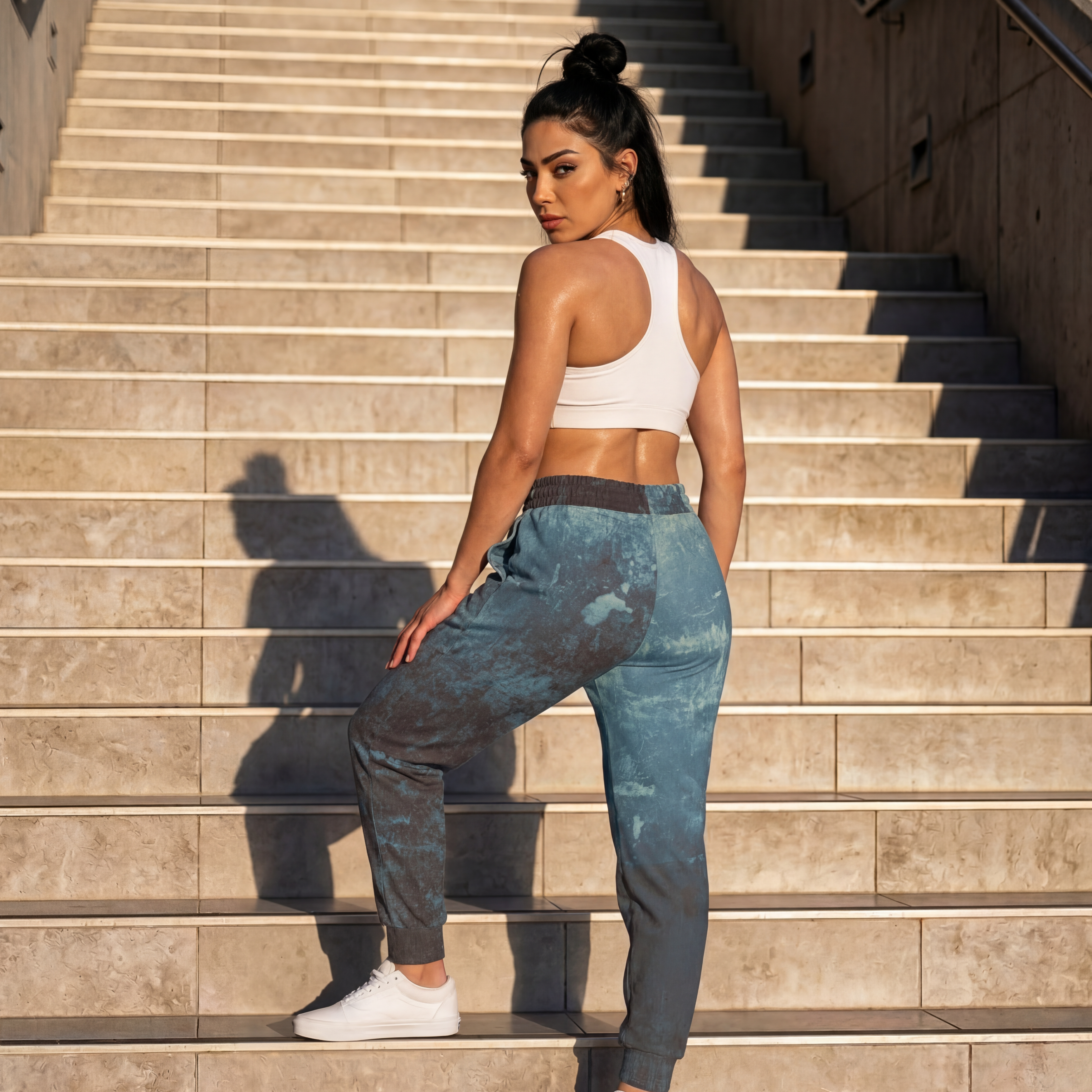 Model wearing distressed athletic sweatpants in blue on outdoor stairs with sporty crop top