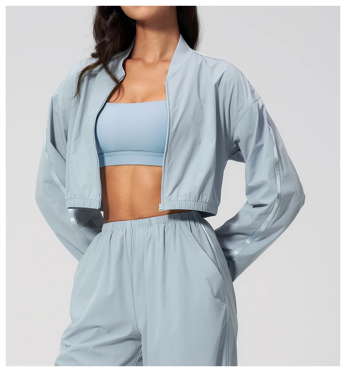Women’s cropped sky blue zip-up jacket with long sleeves over a sports bra.
