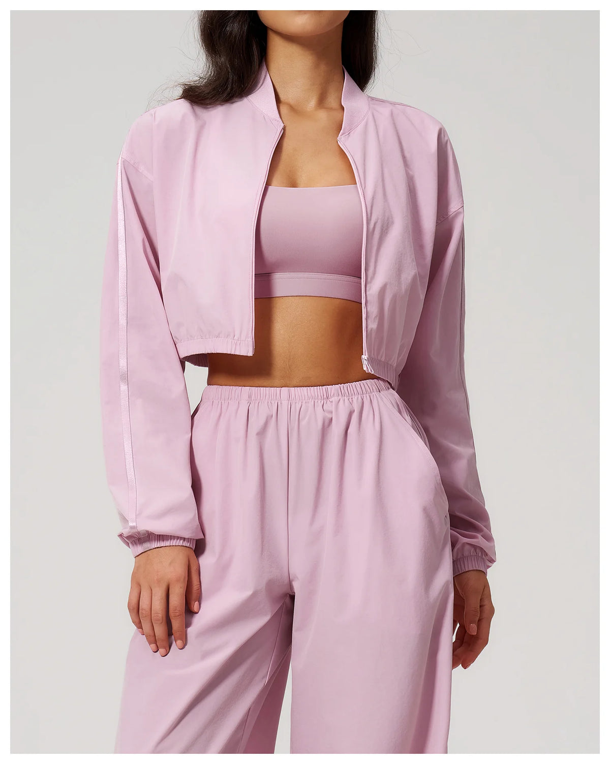 Women’s light pink cropped zip jacket layered over sports bra and matching pants.