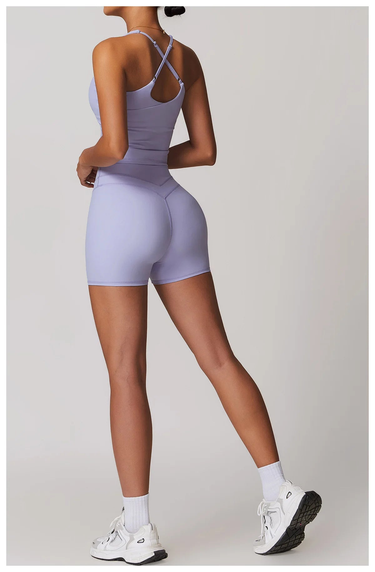 Back view of woman wearing Xooie Fit fitness tank top and biker shorts set in light purple with white sneakers