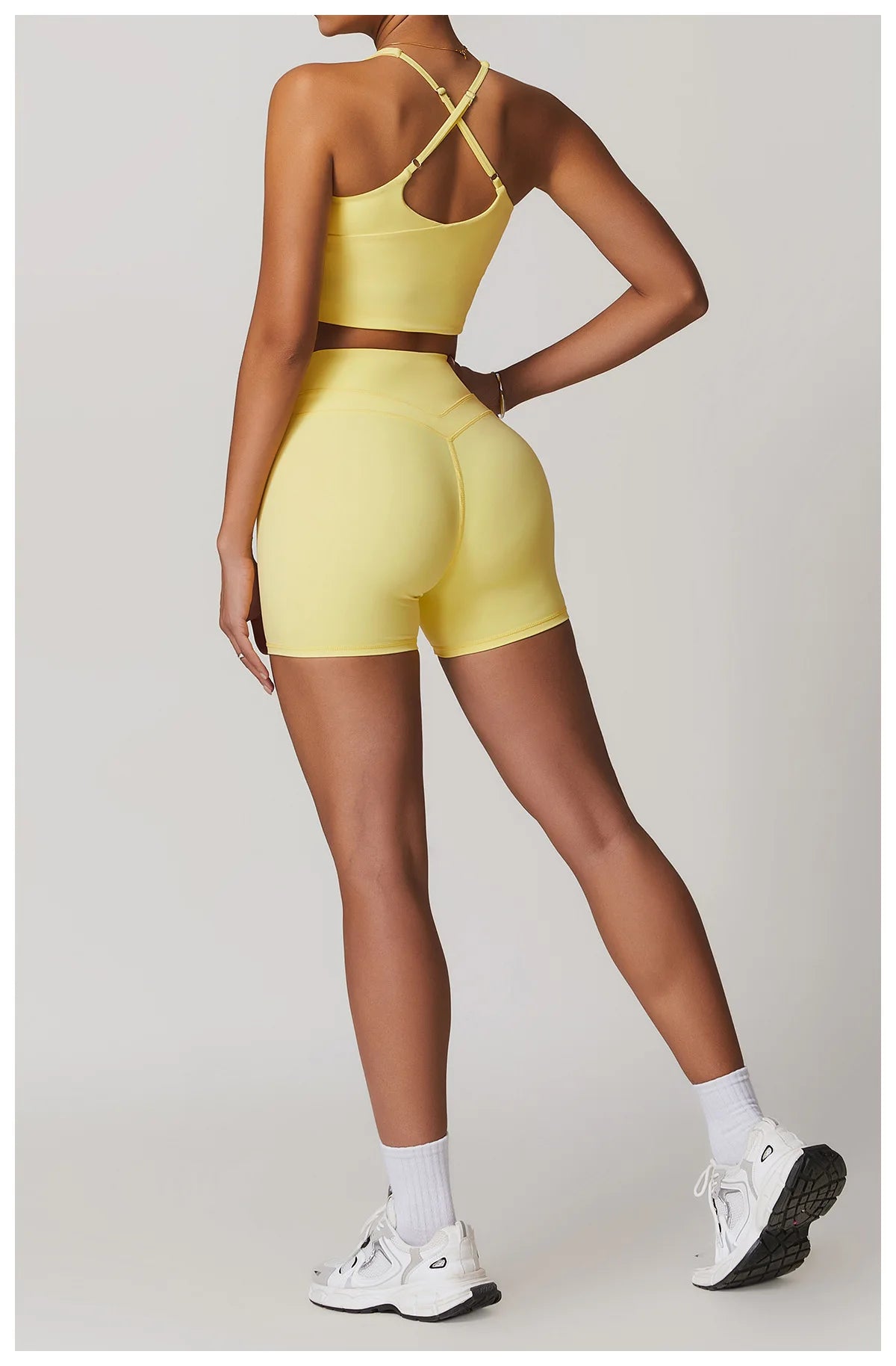 Back view of woman wearing yellow fitness tank top and biker shorts set with white sneakers