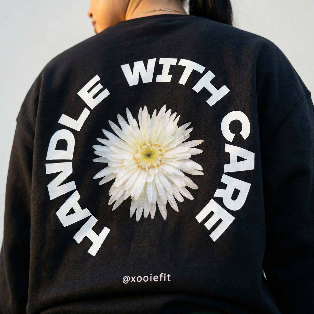Black crewneck sweatshirt back close-up: white daisy with circular "WITH CARE" text