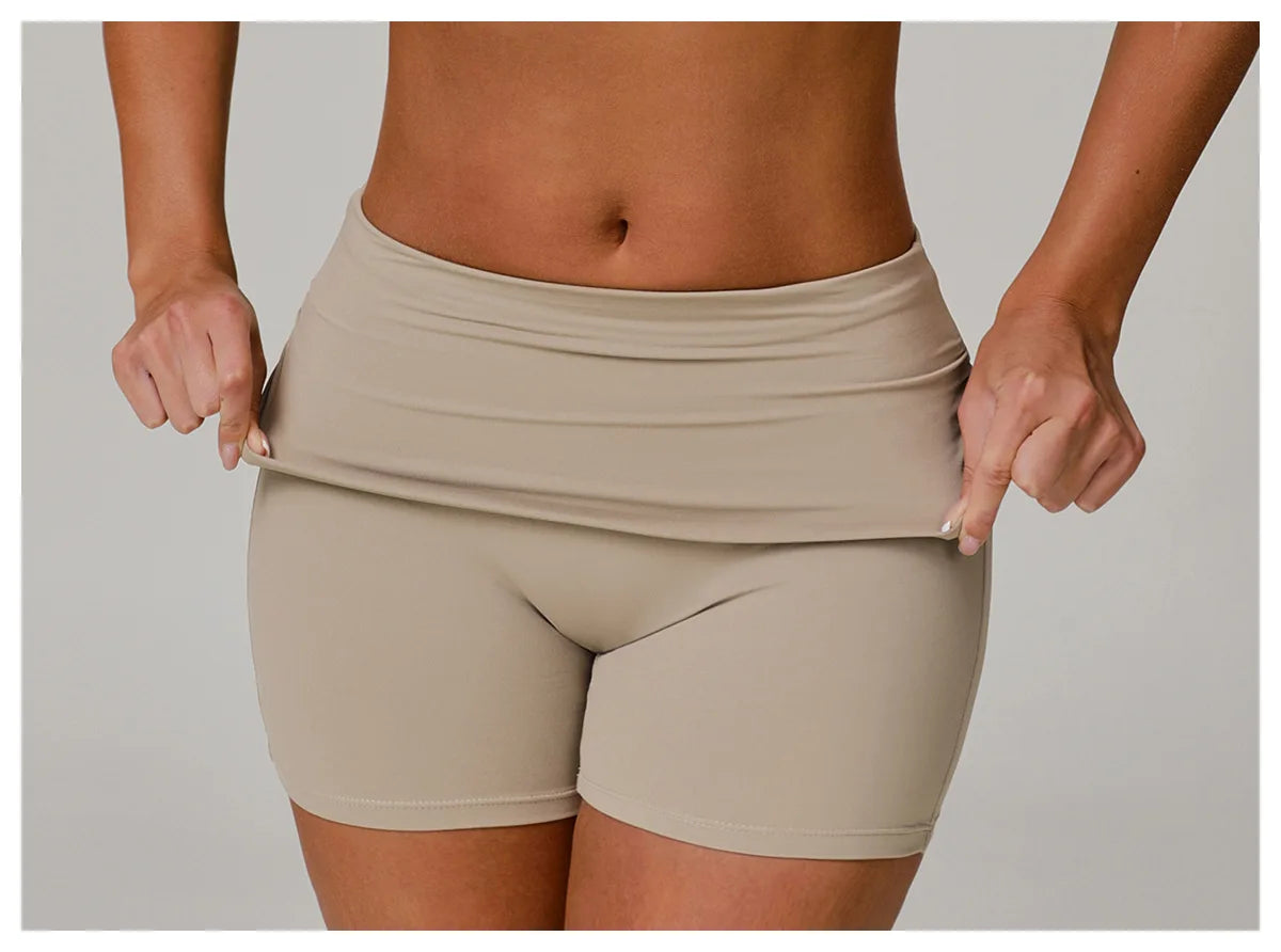 Xooie Fit beige foldable waistband yoga shorts shown on model stretching waistband