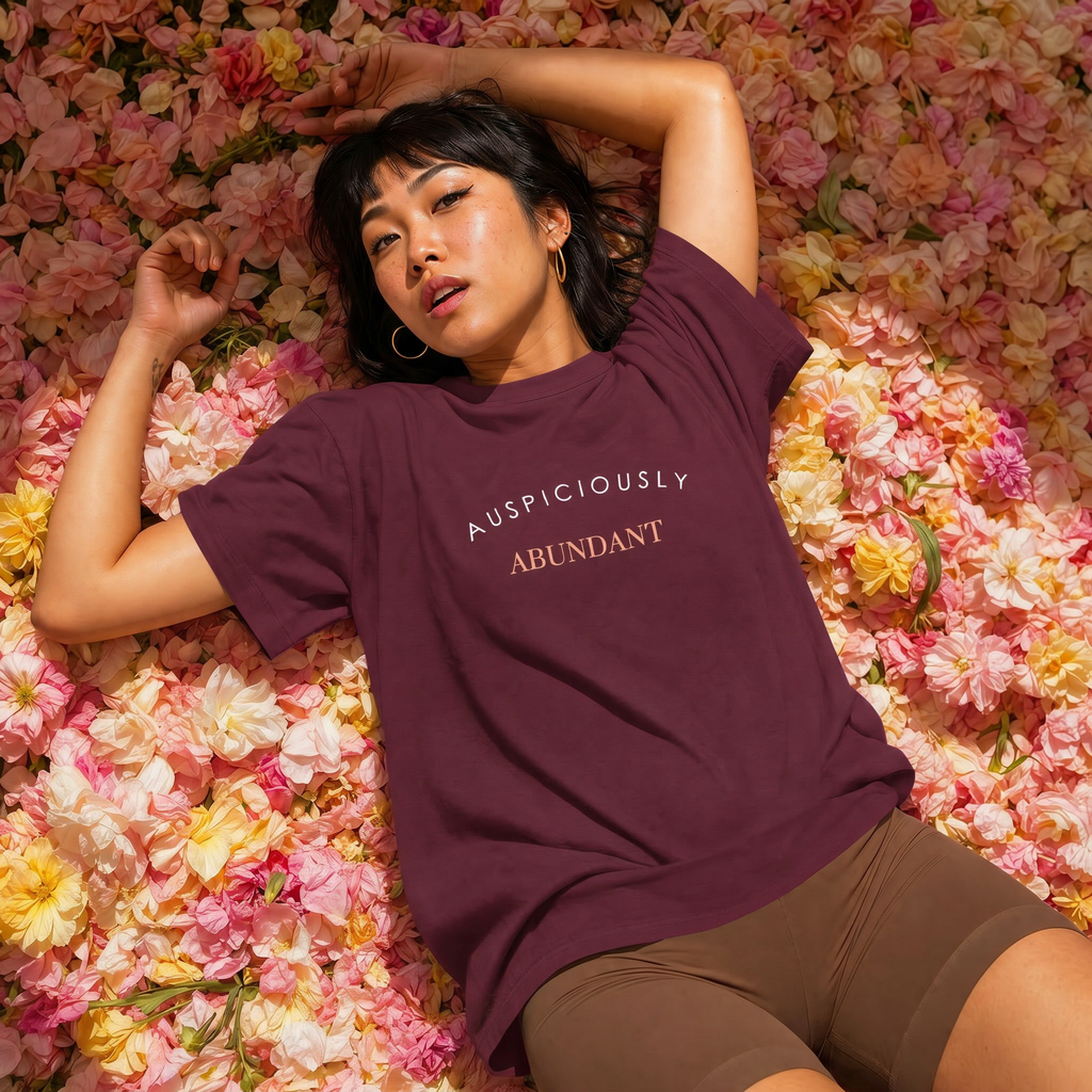 Burgundy crewneck T-shirt with “AUSPICIOUSLY ABUNDANT” text graphic on the front.