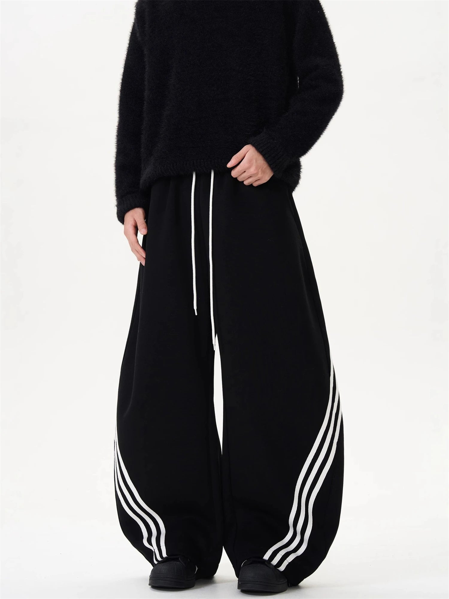 Black oversized sweatpants with white striped side panels and dangling drawstring ties.