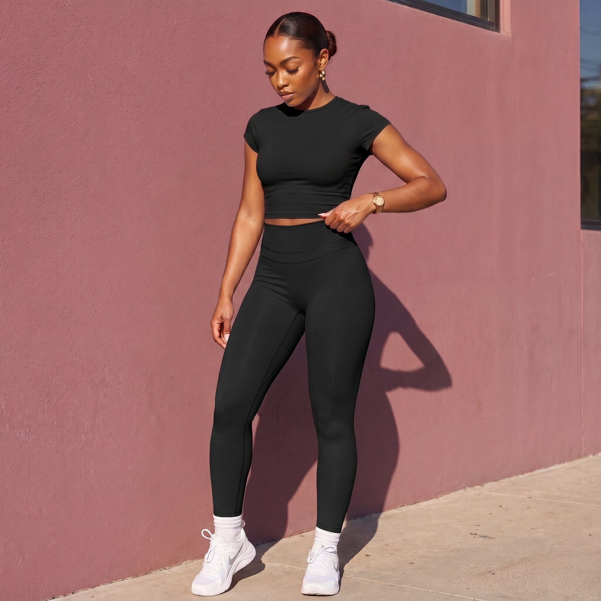 Woman in black athletic outfit standing against a pink wall