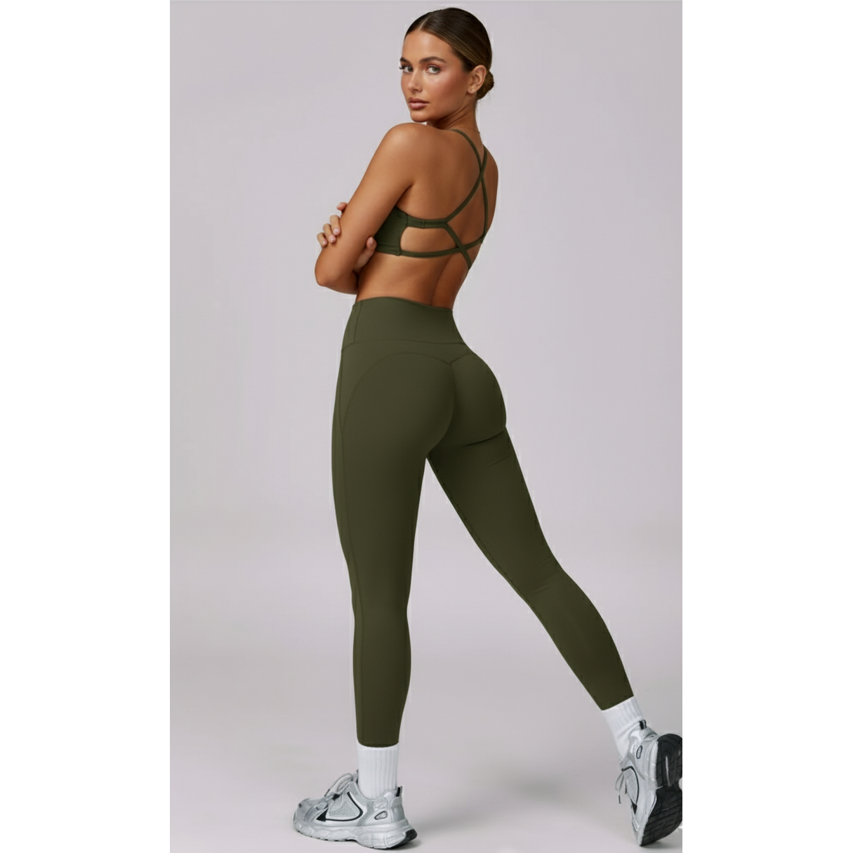 Woman wearing green athletic leggings and sports bra on a light gray background