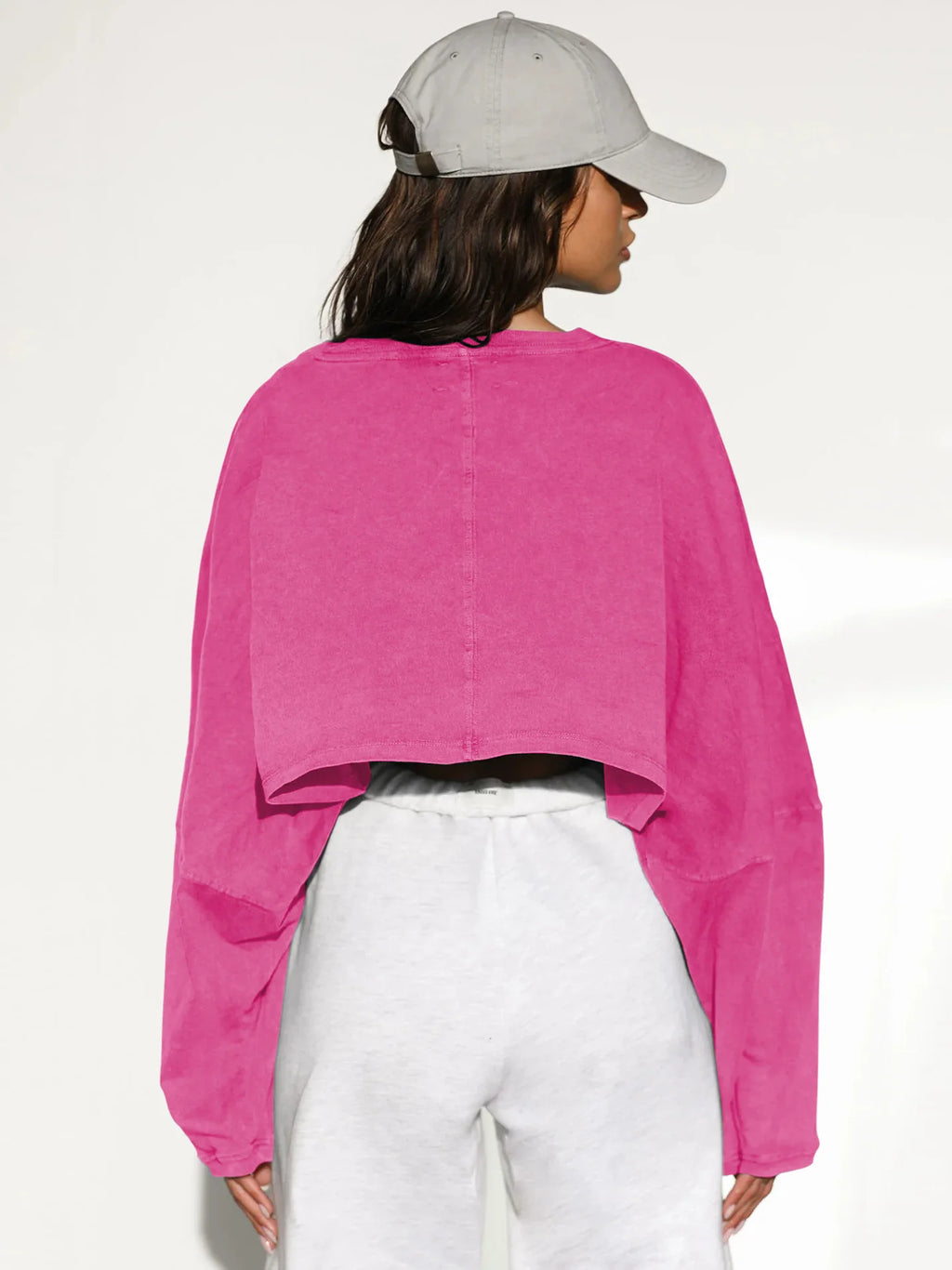 Back view of a pink women's baggy crop top from Xooie Fit, styled with a grey cap and white pants