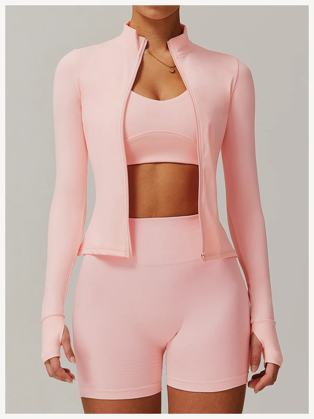 Xooie Fit women's fitness jacket with thumb holes in light pink worn with matching shorts and sports bra