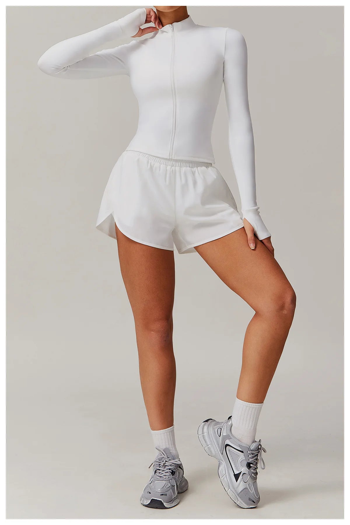 Xooie Fit women's fitness jacket with thumb holes in white paired with white athletic shorts and sneakers
