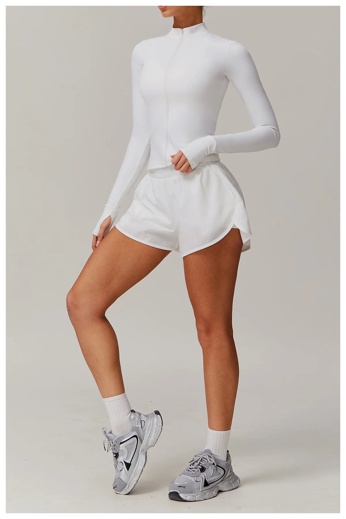 Xooie Fit women's fitness jacket with thumb holes in white, paired with white shorts and gray running shoes