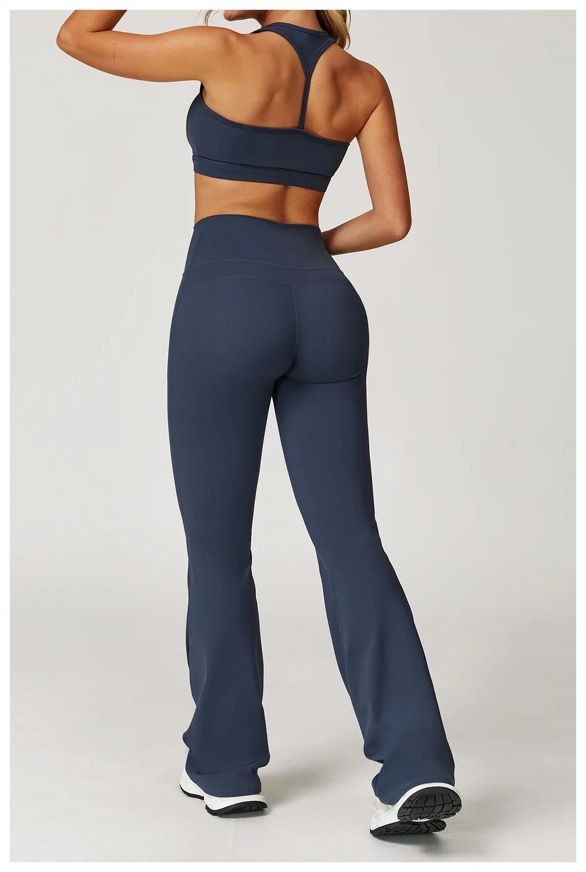 Xooie Fit women's workout set flared pants in dark blue modeled from the back with a matching sports bra