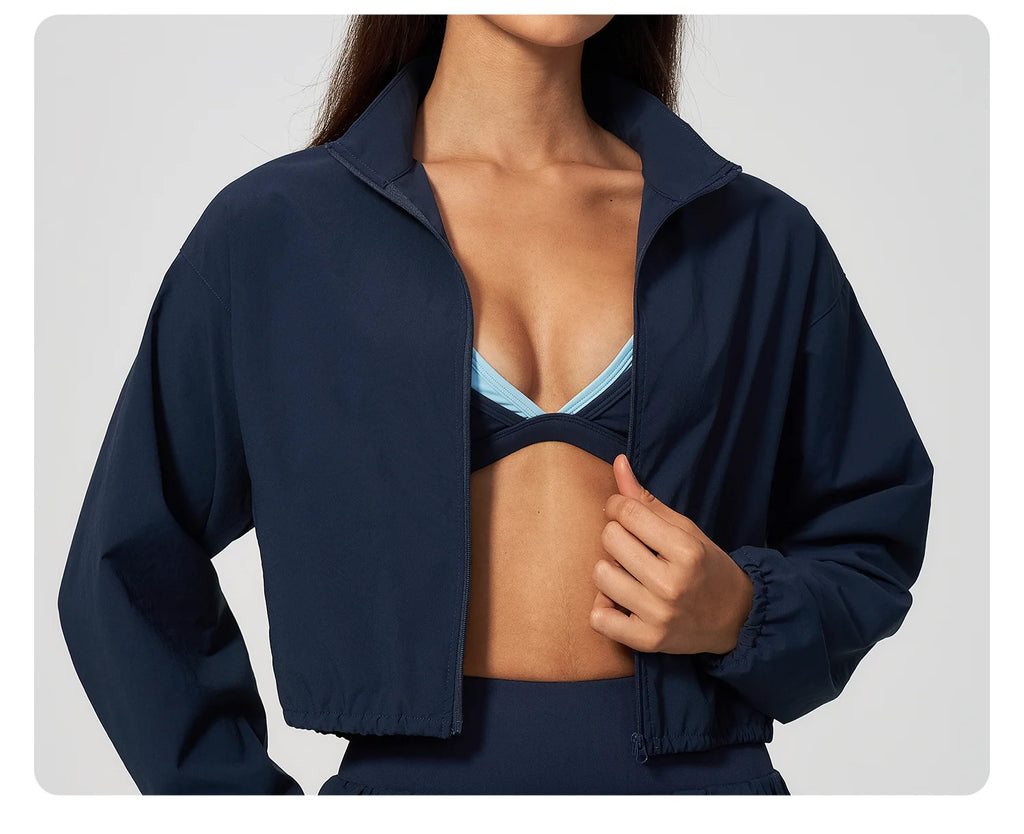 Navy zip-up jacket worn over sports bra, with high collar and elastic cuffs